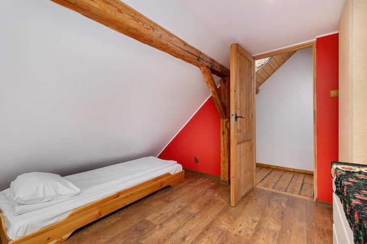 Un dormitorio similar en el ático con camas colocadas bajo vigas de madera inclinadas. La pared azul añade profundidad al espacio luminoso.