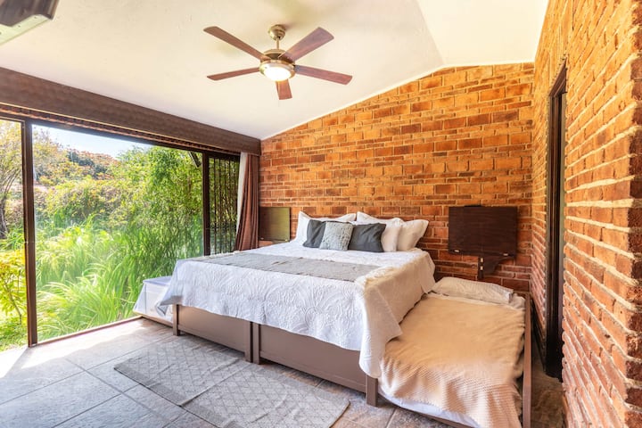 Este dormitorio combina texturas rústicas con vistas directas al jardín, complementadas con una disposición flexible para dormir.