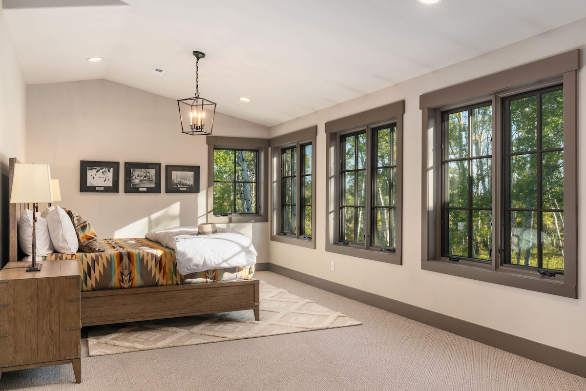 Suite principal con ventanas envolventes y vistas al bosque. Despiértate con la luz del sol que fluye a través de los álamos.