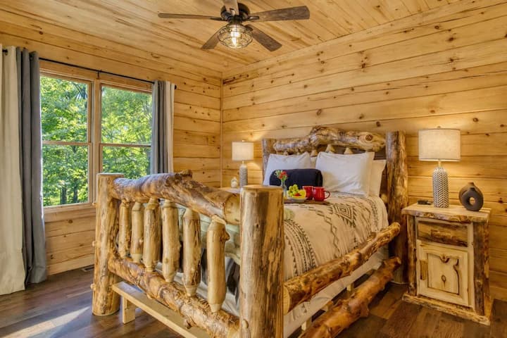 Chambre queen de plain-pied avec lit en rondins authentique, linge de lit de luxe et vue magnifique sur la montagne : le confort rencontre l'élégance rustique.
