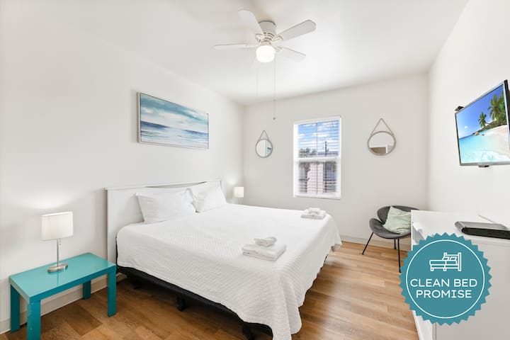 Descansa tranquilamente en tu luminoso dormitorio con arte costero, ventilador de techo y televisor moderno para tu comodidad.
