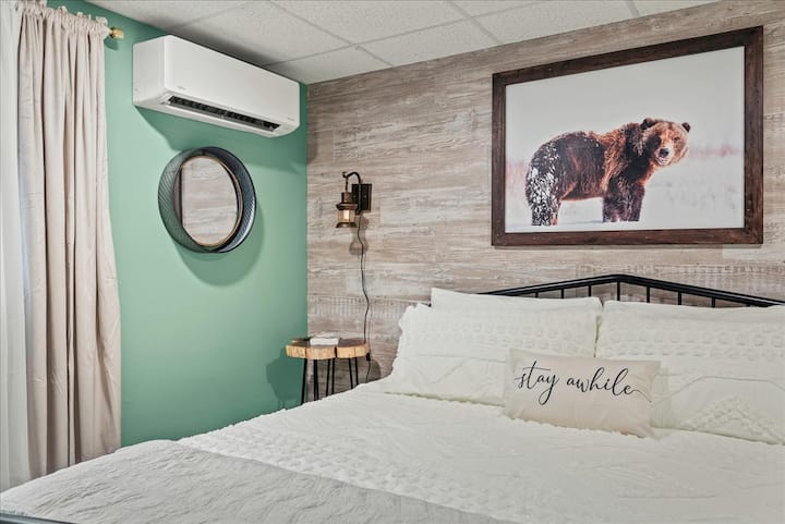 Спална соба 4: овој пријатен апартман со голем брачен кревет има меки ѕидови во боја на жалфија со топли дрвени тонови и перница со натпис „Останете уште малку“ – мирно потсетување дека тука треба да се забавите.