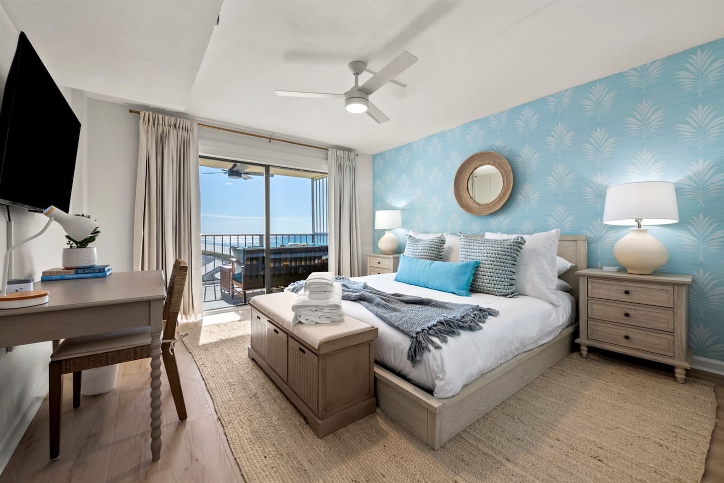 Bedroom one with a king bed, coastal blue decor and a desk beside the balcony door