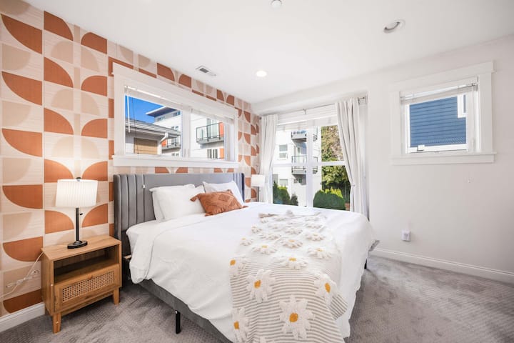 Útulná spálňa s veľkou manželskou posteľou, veľkými oknami a modernými prvkami.