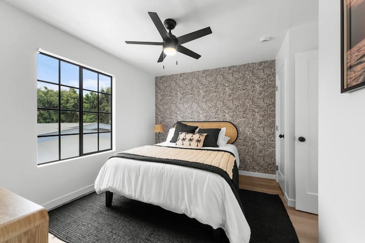 Táto útulná spálňa má manželskú posteľ, výraznú akcentovanú stenu a výhľad na okno lemované stromami. Upokojujúci priestor v modernom pobrežnom Airbnb Crown Point – ideálny na oddych po slnečnom dni v San Diegu pri zálive.