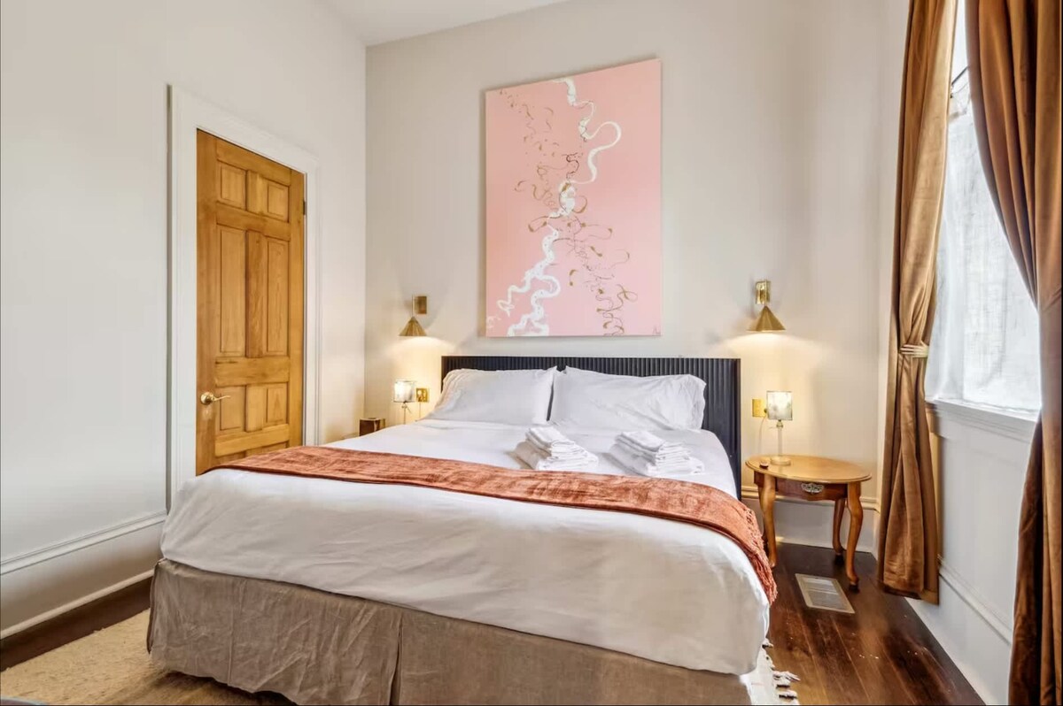 时尚的卧室，配备加大双人床和柔和的粉红色艺术品中心。