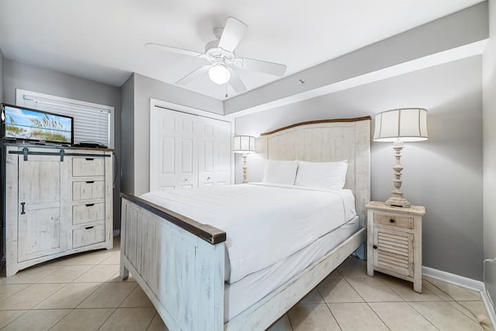 Cama king cómoda con sábanas blancas y frescas, flanqueada por mesitas de noche y lámparas a juego, y complementada con prácticas soluciones de almacenamiento, lo que crea un espacio acogedor y atractivo.