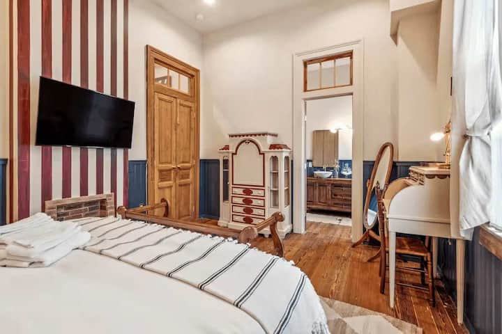 Dormitorio tamaño king con pared a rayas, escritorio y acceso al baño privado.