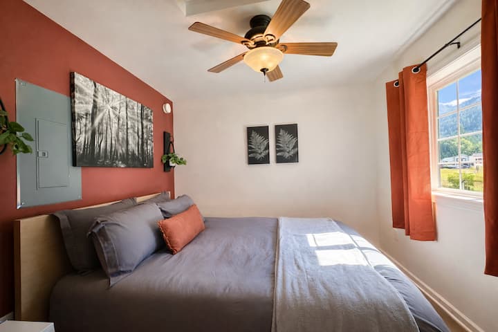 Tu acogedor dormitorio cuenta con una cómoda cama, un suave ventilador de techo y vistas a la montaña a través de ventanas luminosas.