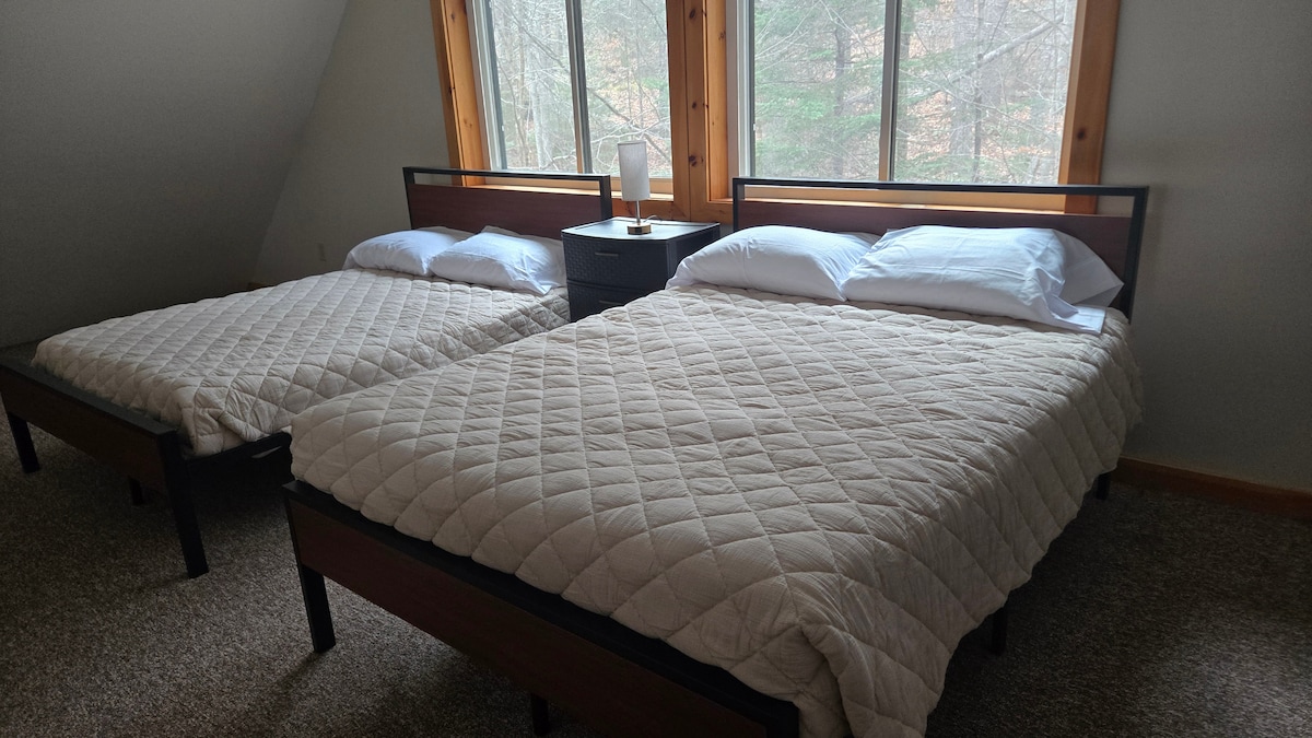 Loftová spálňa s dvoma plnými posteľami a veľkými oknami.