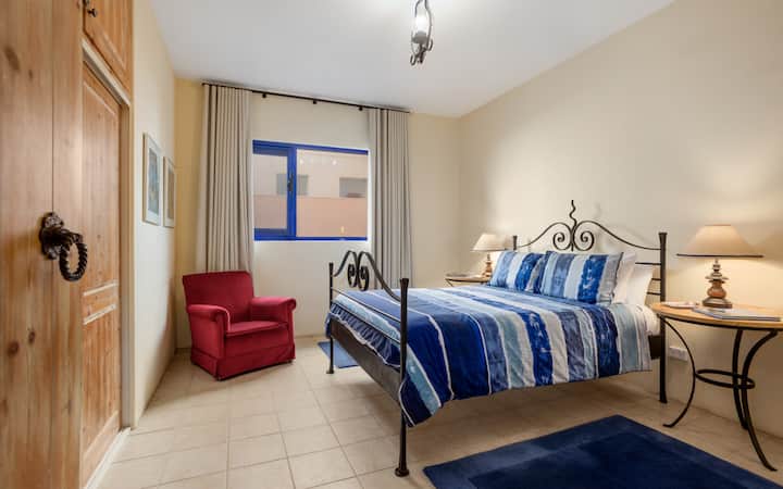 Pumzika kwenye chumba kikuu cha kutuliza ambapo kitanda aina ya queen, rangi laini na sauti za bahari huhimiza kupumzika kabisa.