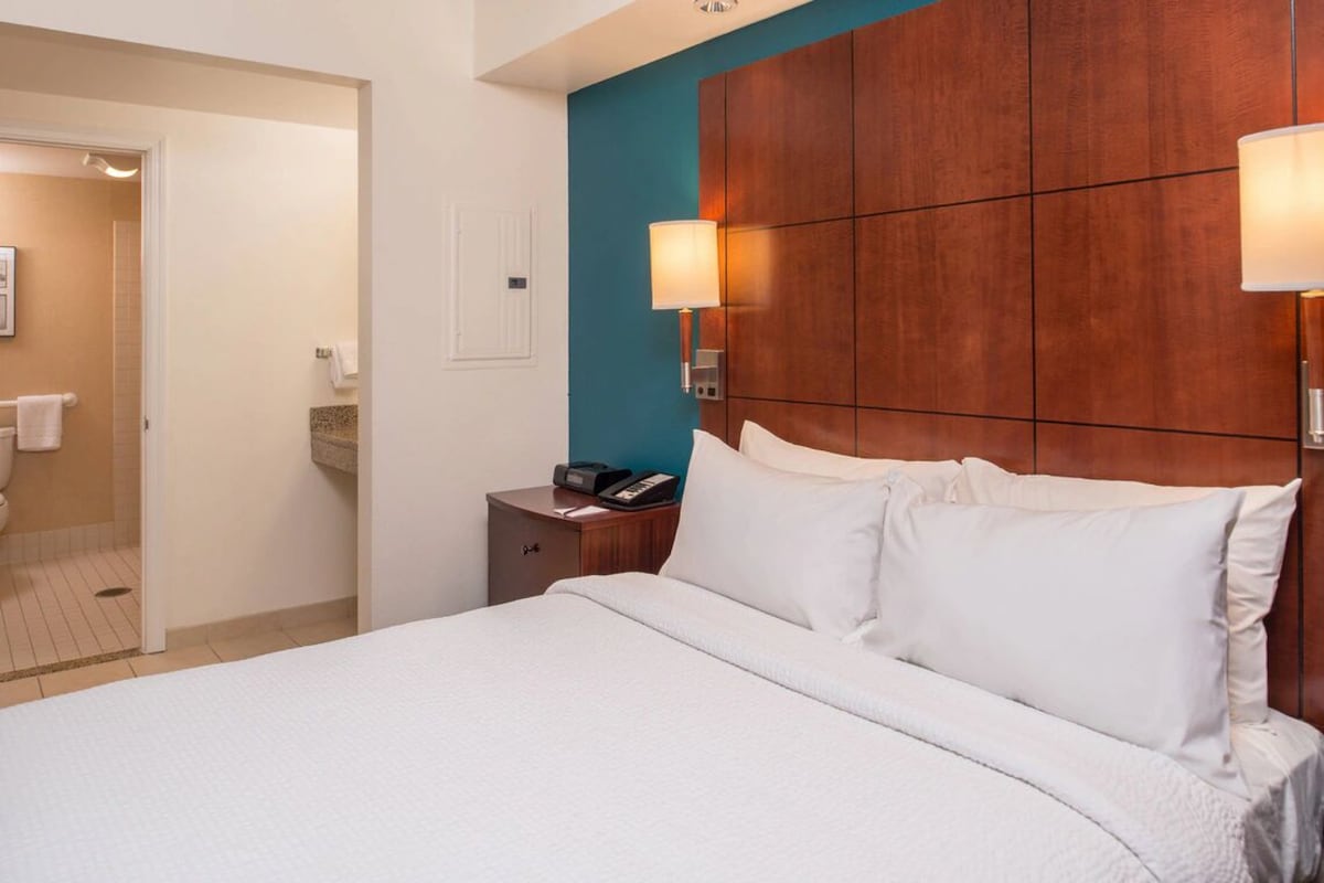 سرير كينج بالقرب من الحمام مع جدار بلون أزرق مخضر وألواح خشبية