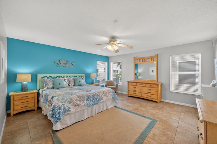 חדר שינה אוורירי עם מצעים בסגנון חוף, שידה לאחסון ומאוורר תקרה לנוחות