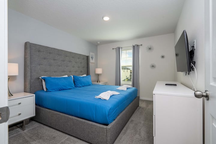 Descansa tranquilo en este elegante dormitorio con una lujosa cama tamaño king, grises y azules relajantes y un televisor montado en la pared para las noches de cine.