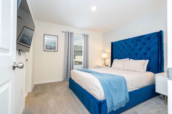 Elegante habitación con cabecero acolchado azul profundo y blancos nítidos: relájate en la cómoda cama tamaño queen, además de TV y alfombra suave.