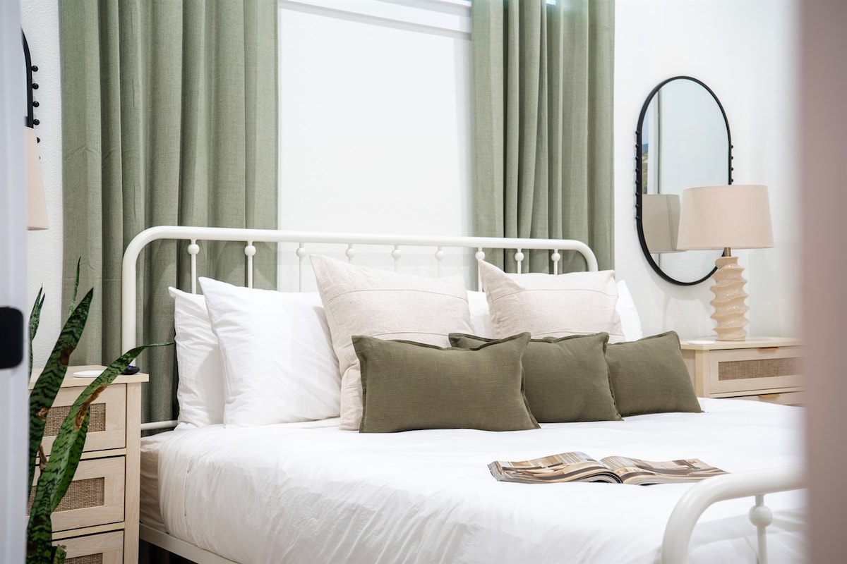 Dhomë gjumi kryesore me perde bojë sherbele dhe kornizë krevati të bardhë hekuri — e qetë, e pastër, gati për pushim