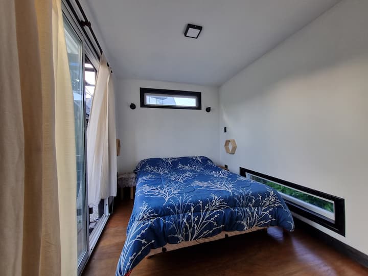 明亮的卧室，可直接通往阳台，可欣赏绿色景观。 其简约的设计和黑色细节突出了环境的清晰度，非常适合在大自然和自然光线的环绕下休息。