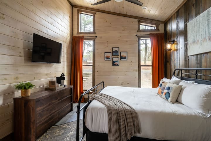 This king-sized bedroom has four windows facing the front of the cabin. They let in plenty of natural light and have shades to help you sleep and give privacy. Enjoy the smart TV, coffee station, and private ensuite bathroom.