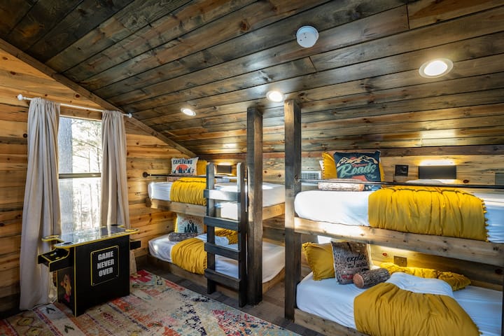 This bedroom features four single bunk beds, each neatly arranged and accented with unique, themed pillows, ideal for a group stay. Each bed has a reading light and electric outlets, perfect for charging devices.