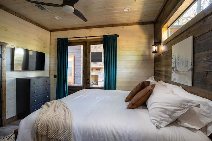 The primary king bedroom has a ceiling fan, a TV, a large natural-light window, and doors that open to the patio, with privacy shades.