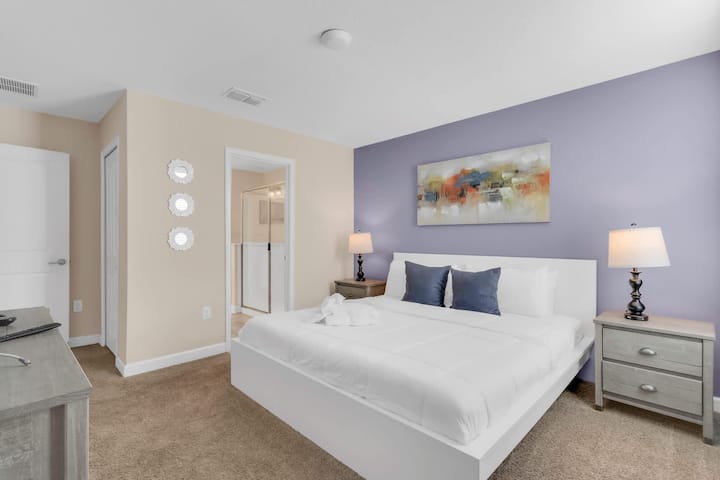 King bedroom with white furniture and colorful wall art.