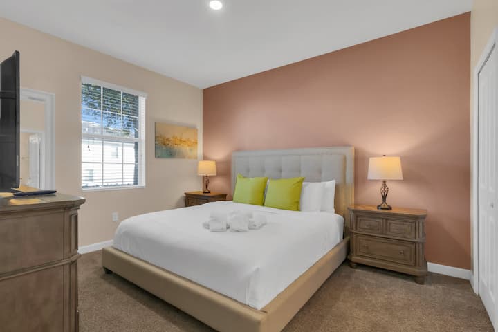 Queen bedroom with wood bed frame and bright accents.
