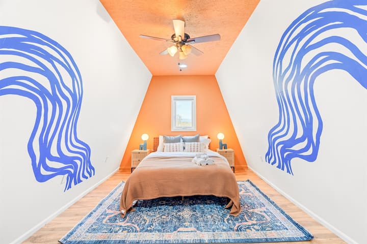 Причудлива пета спалня с двойно легло, вентилатор на тавана, стенописи с вълни и топло осветление – уникален, уютен кът, идеален за самостоятелни пътници или двойки, търсещи артистичен чар.