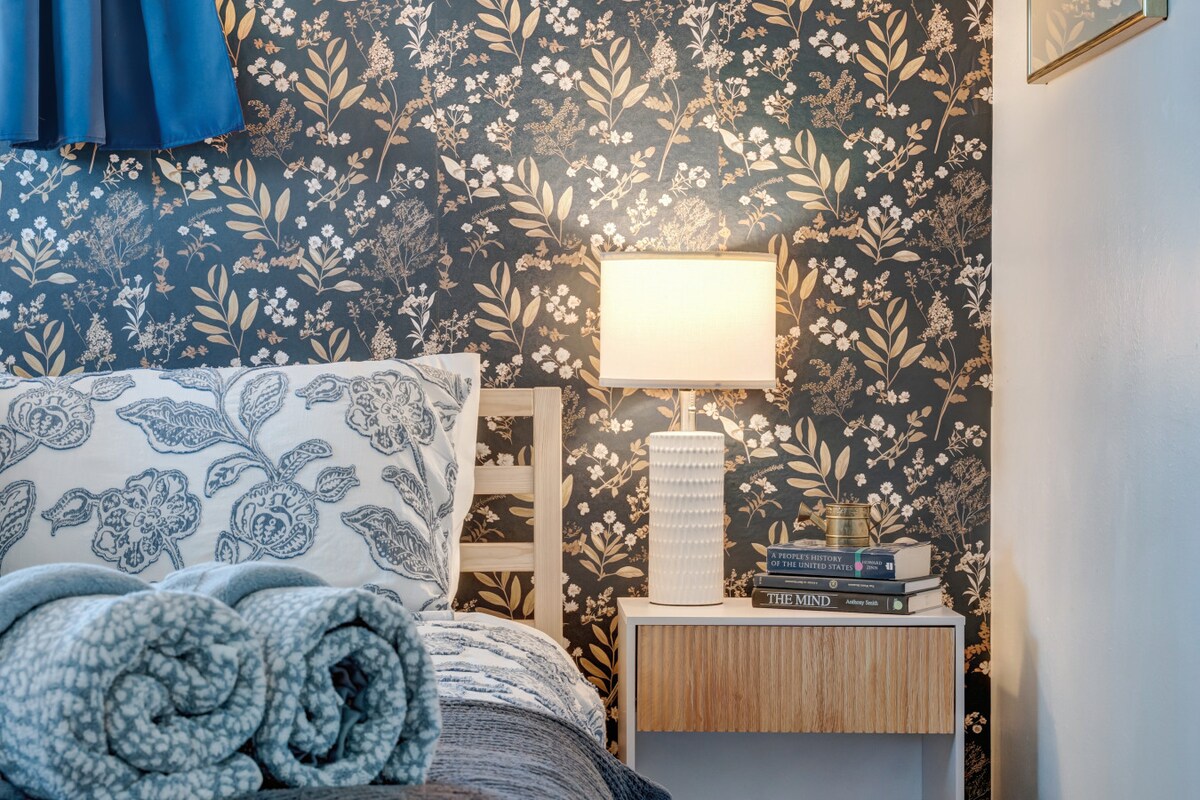 استمتع بنوم هانئ في غرفة نوم مستوحاة من الأزهار مصممة بألوان هادئة وبياضات ناعمة وإضاءة دافئة بجانب السرير.