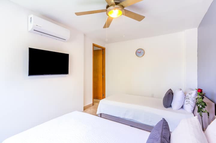 ห้องนอนสไตล์มินิมอลพร้อมทีวีติดผนัง พัดลมเพดาน และการออกแบบที่สะอาดและทันสมัย