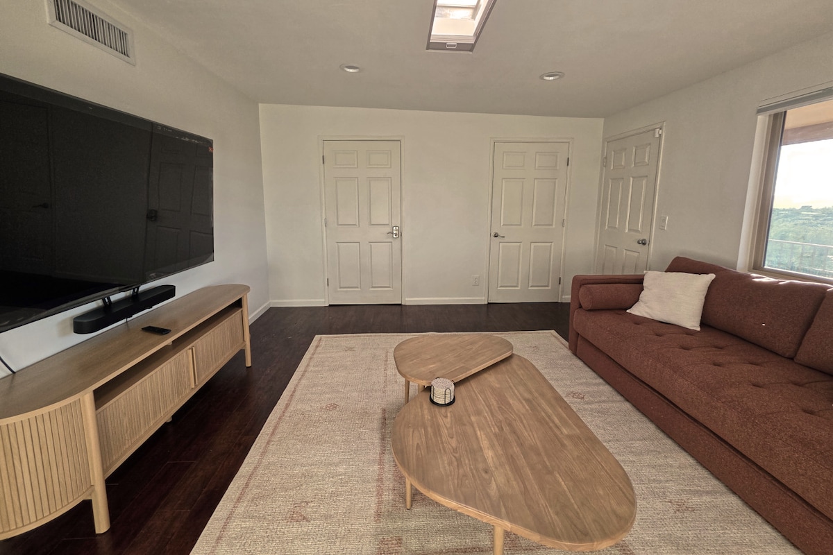 Fleksibilna spavaća soba na glavnoj razini s kaučem na razvlačenje, velikim HD televizorom i pristupom trijemu s pogledom na bazen i zalazak sunca.