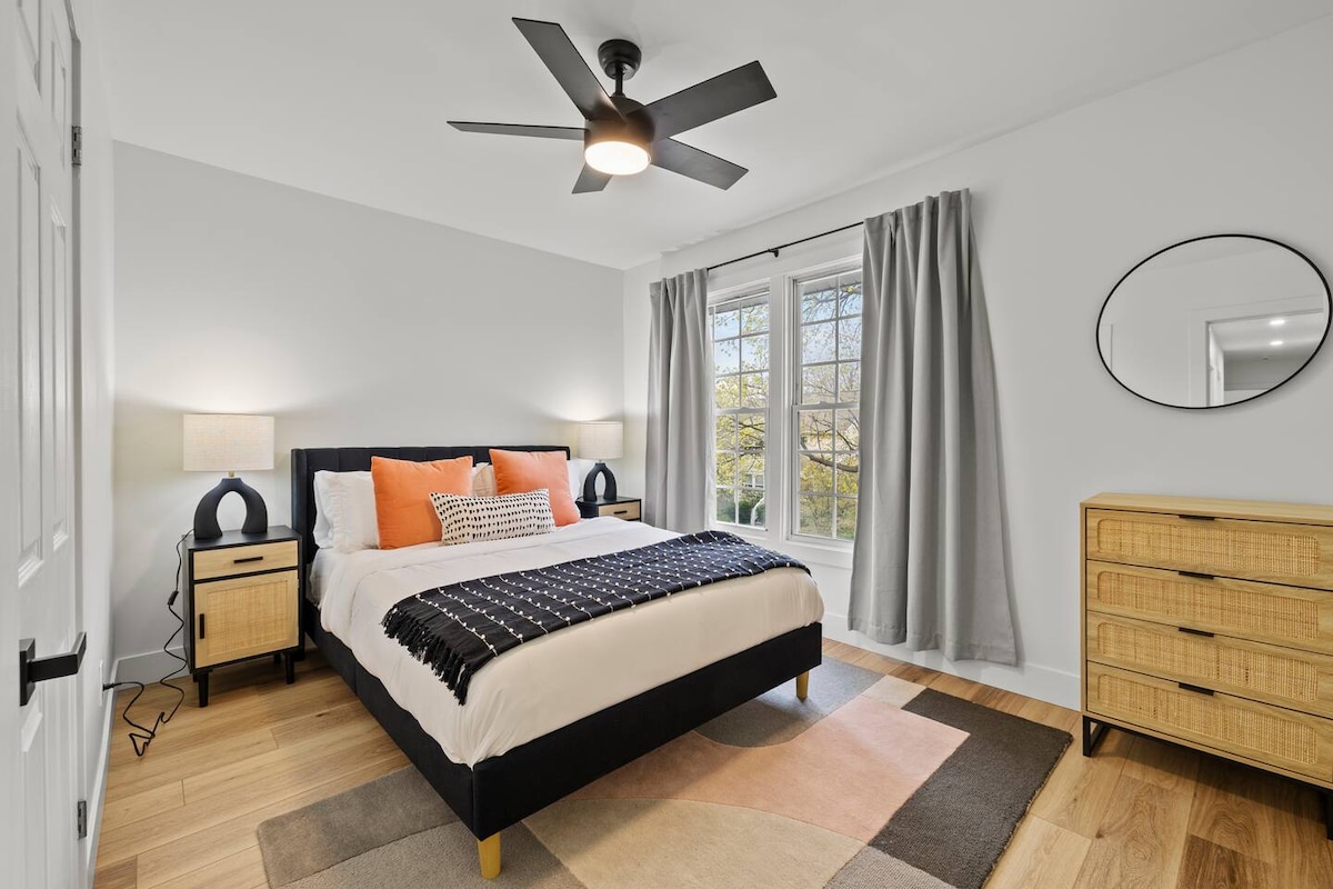 غرفة نوم مريحة وأنيقة تتميز بسرير بحجم كوين وستائر تعتيم سميكة لقضاء ليلة مريحة. تتضمن هذه المساحة المشرقة مروحة سقف وخزانة أدراج من الروطان ومناضد سرير جانبية حديثة مع مصابيح للقراءة.