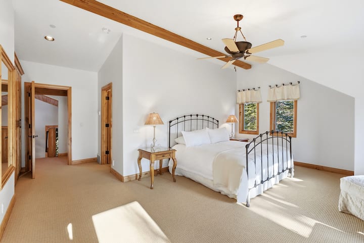 Dormitor rustic cu cadru de pat din fier, lenjerie de pat ușoară și ornamente din lemn cald, creând o atmosferă confortabilă de refugiu montan.