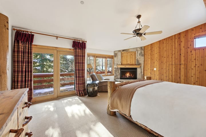 Dormitor confortabil cu ferestre mari care oferă priveliști pitorești, pereți cu lambriuri din lemn, un pat king-size și ventilator de tavan