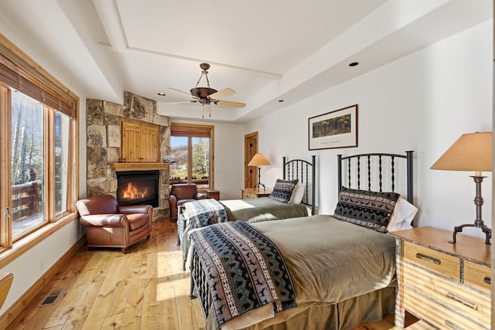 Dormitor în stil rustic, cu șemineu în colț, mobilier din lemn și uși glisante din sticlă care duc spre un balcon privat cu vedere la munte.