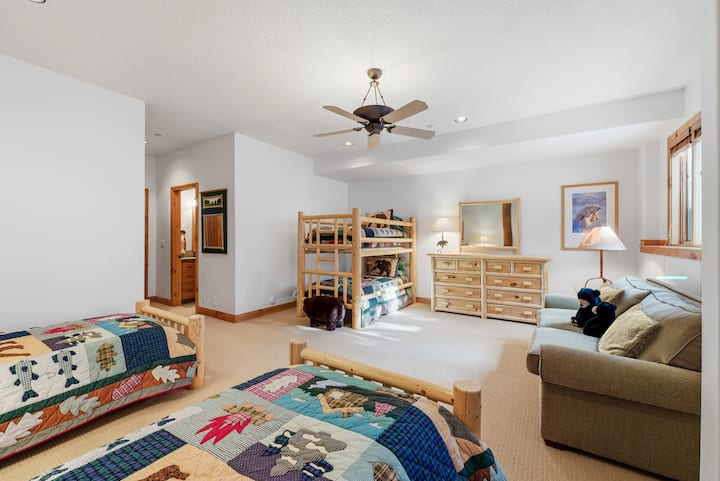 Dormitor confortabil cu două paturi twin cu pilote patchwork, ventilator de tavan și o mică zonă de relaxare cu canapea și fotoliu.