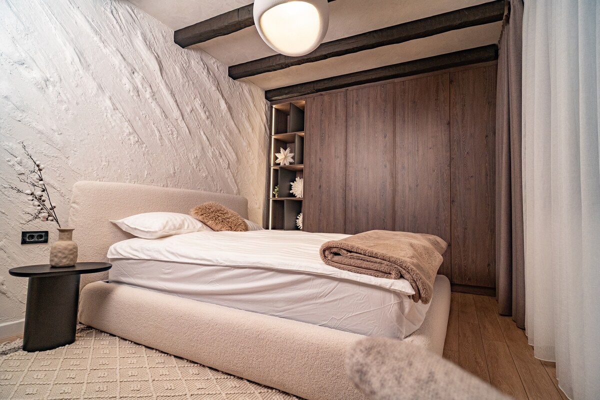 Breed slaapkamerzicht met opbergruimte op maat, zichtbare balken en een rustgevend neutraal palet. Een verfijnde mix van modern comfort en op de bergen geïnspireerd design, ideaal om tot rust te komen in totale privacy.