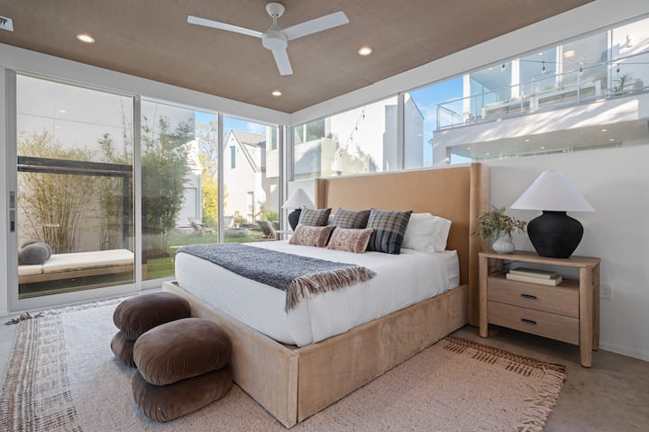 Chumba cha kulala cha msingi chenye kitanda cha mbao, dari iliyoinama na milango ya kioo kutoka sakafuni hadi dari.