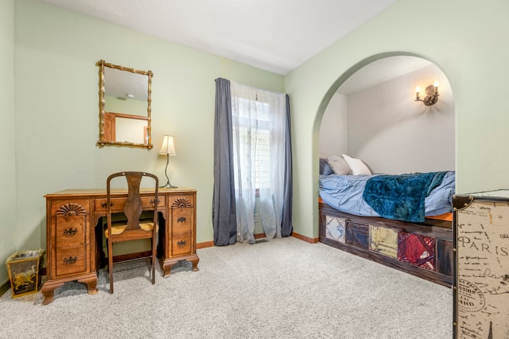 Útulná posteľ vo výklenku + stôl v retro štýle v svetlom ubytovaní s kobercom