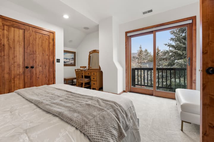 Slnečná spálňa s balkónom a výhľadom na koruny stromov, rustikálne drevené prvky.