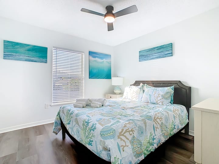 غرفة نوم ساحلية مع أعمال فنية ومصابيح دافئة بجانب السرير.