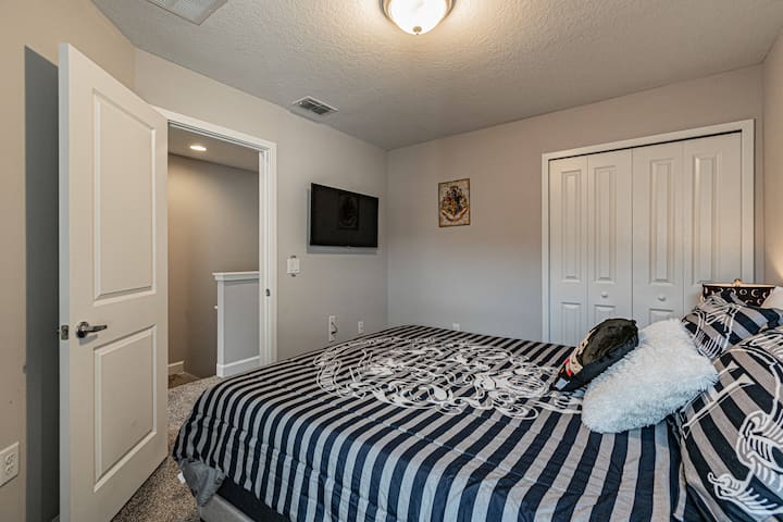 Relájate en un acogedor dormitorio con un elegante edredón a rayas y texturas suaves. Disfruta del ambiente relajante creado por la iluminación ambiental y las paredes grises sutiles, junto con un televisor montado para relajarte después de tus aventuras.