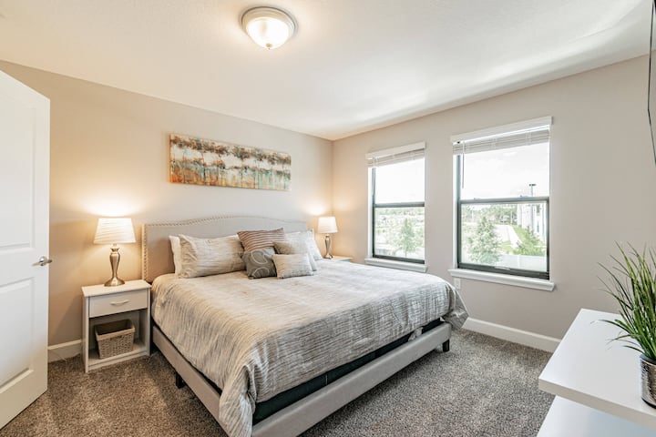 Este dormitorio luminoso ofrece una lujosa cama en tonos neutros con almohadas texturizadas y elegantes lámparas de cabecera para un ambiente cálido. Las grandes ventanas dejan entrar la luz natural y ofrecen una vista refrescante, perfecta para una estadía tranquila.