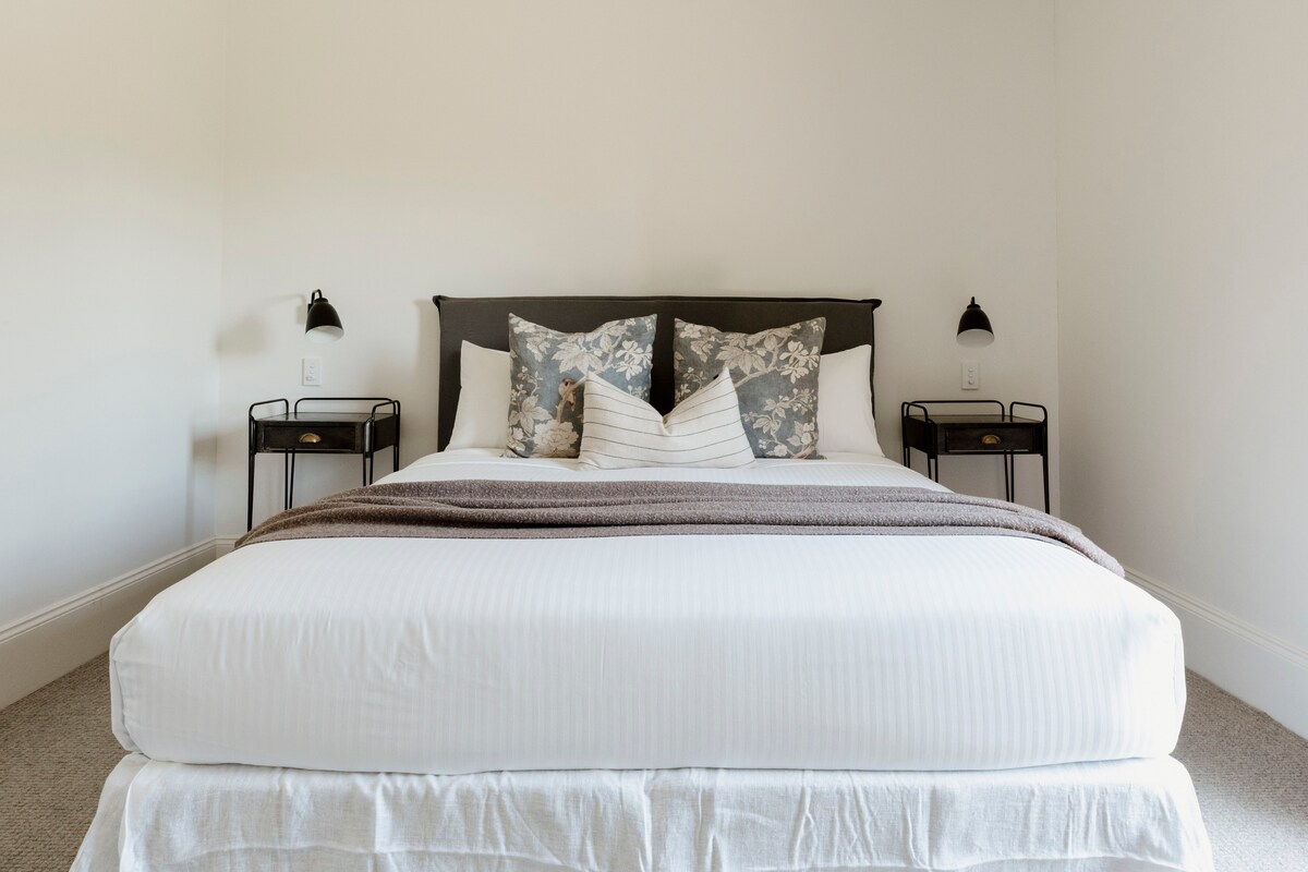 בחדר השינה הראשי יש מיטת קינג סייז עם מצעים נקיים, עם תאורה חמימה ועיצוב רגוע שיוצרים פינה שלווה.