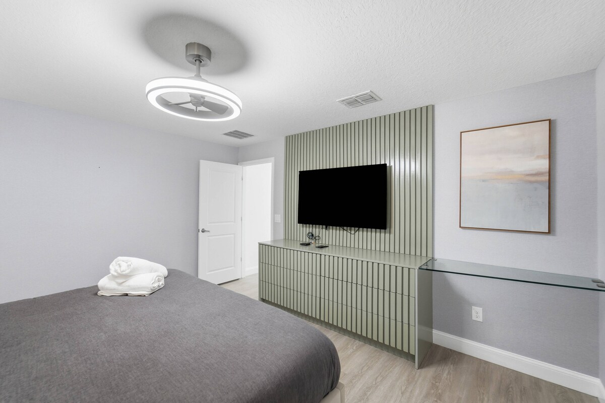 Disfruta de un dormitorio elegante con una acogedora cama tamaño king, sábanas suaves y una elegante pared decorativa que enmarca un televisor montado en la pared. La decoración minimalista y la iluminación cálida crean un ambiente relajante para tu estadía.