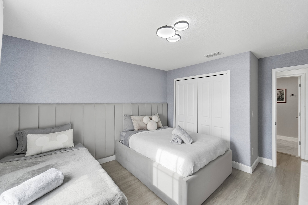 Experimenta la tranquilidad en este dormitorio sereno con dos camas acogedoras vestidas con sábanas suaves, paredes azules claras relajantes y elegantes detalles de madera. La luz natural inunda el espacio, ofreciendo un ambiente luminoso y aireado para noches de descanso.