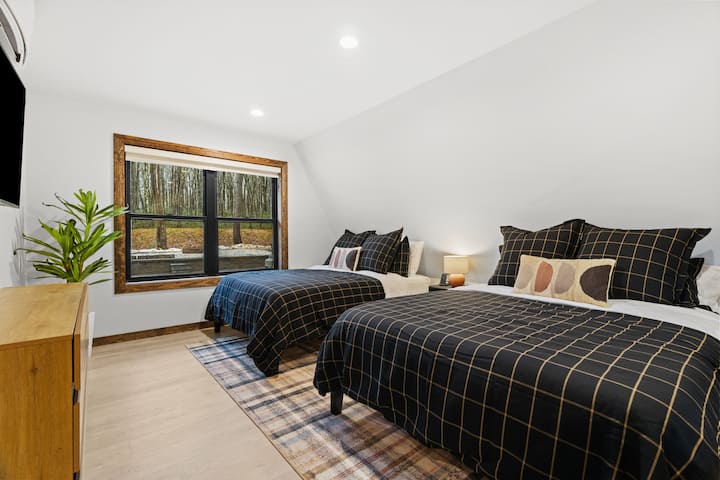 第一间卧室度假屋，有两张舒适的床，透过大窗户可以看到森林景观