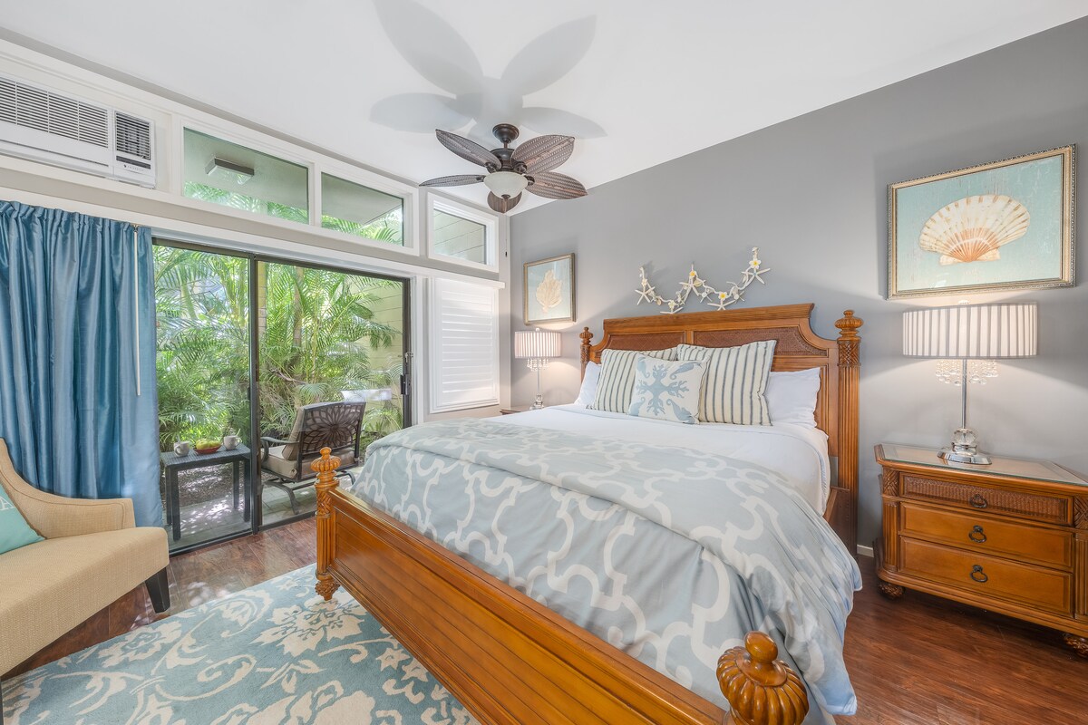 Ontspan in een lichte slaapkamer met een gesneden houten bedframe, zacht beddengoed met een patroon en grote ramen met uitzicht op de weelderige tuin.