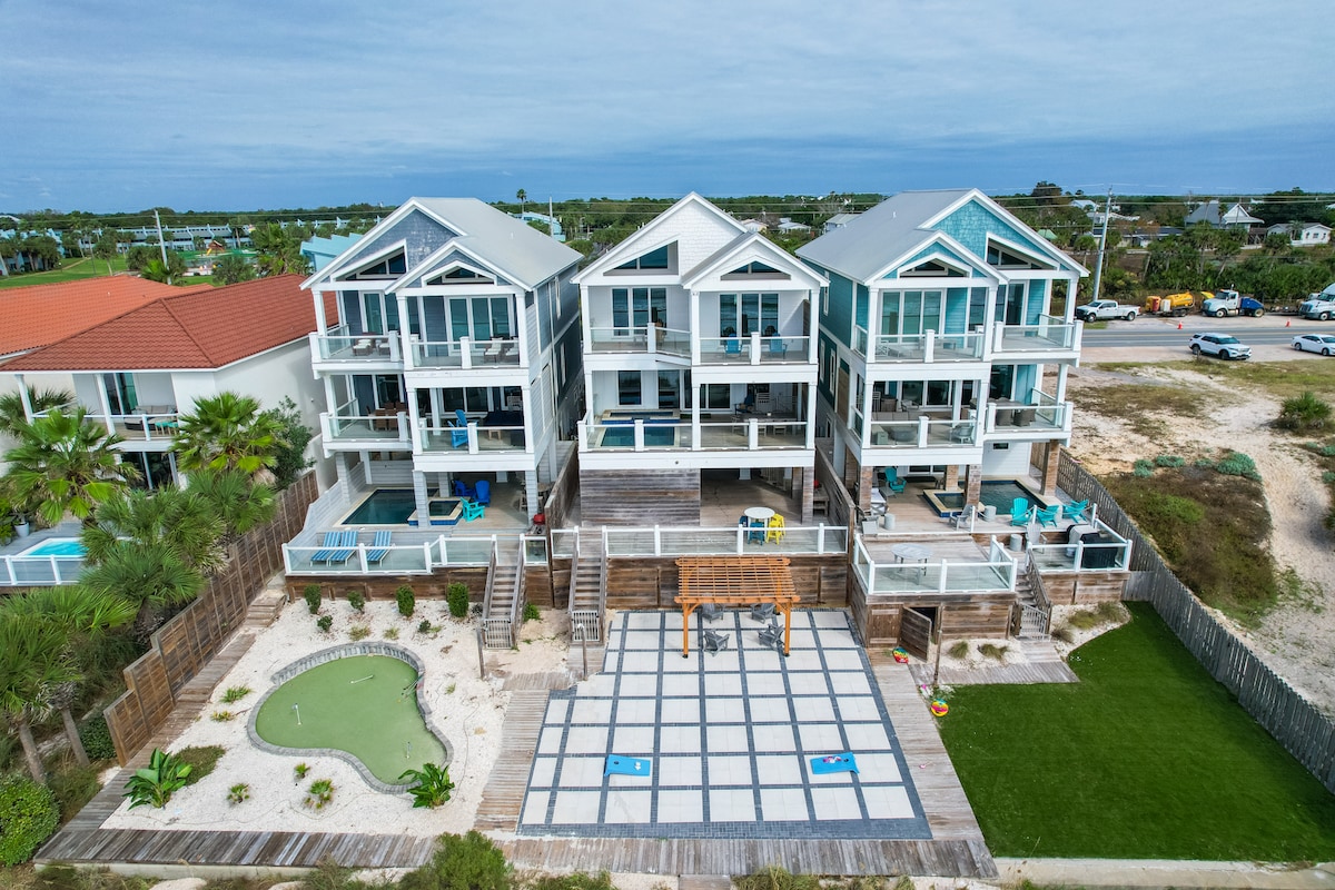 Aerial view of a three-story beachfront home showcases spacious balconies with seating and beach access. A private pool with lounge chairs is visible, along with a manicured yard featuring a mini-golf area. The surrounding landscape includes palm trees and outdoor dining options.