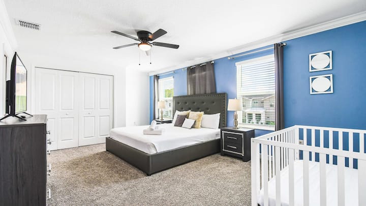 ห้องนอนใหญ่กว้างขวางพร้อมเตียงคิงไซส์ ผนังสีฟ้าสงบ เตียงเด็กเล็ก สมาร์ททีวี และแสงธรรมชาติ
