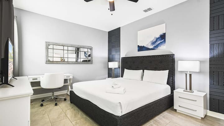 ห้องนอนทันสมัยพร้อมเตียงคิงไซส์ ผนังตกแต่งอย่างมีสไตล์ โต๊ะทำงาน ทีวี และการตกแต่งที่เงียบสงบ
